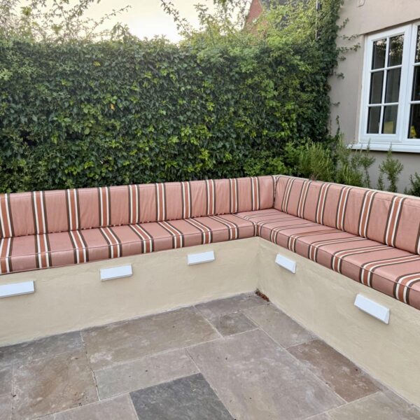 Bespoke outdoor bench seating cushions in striped fabric for an L-shaped built-in garden seating area.