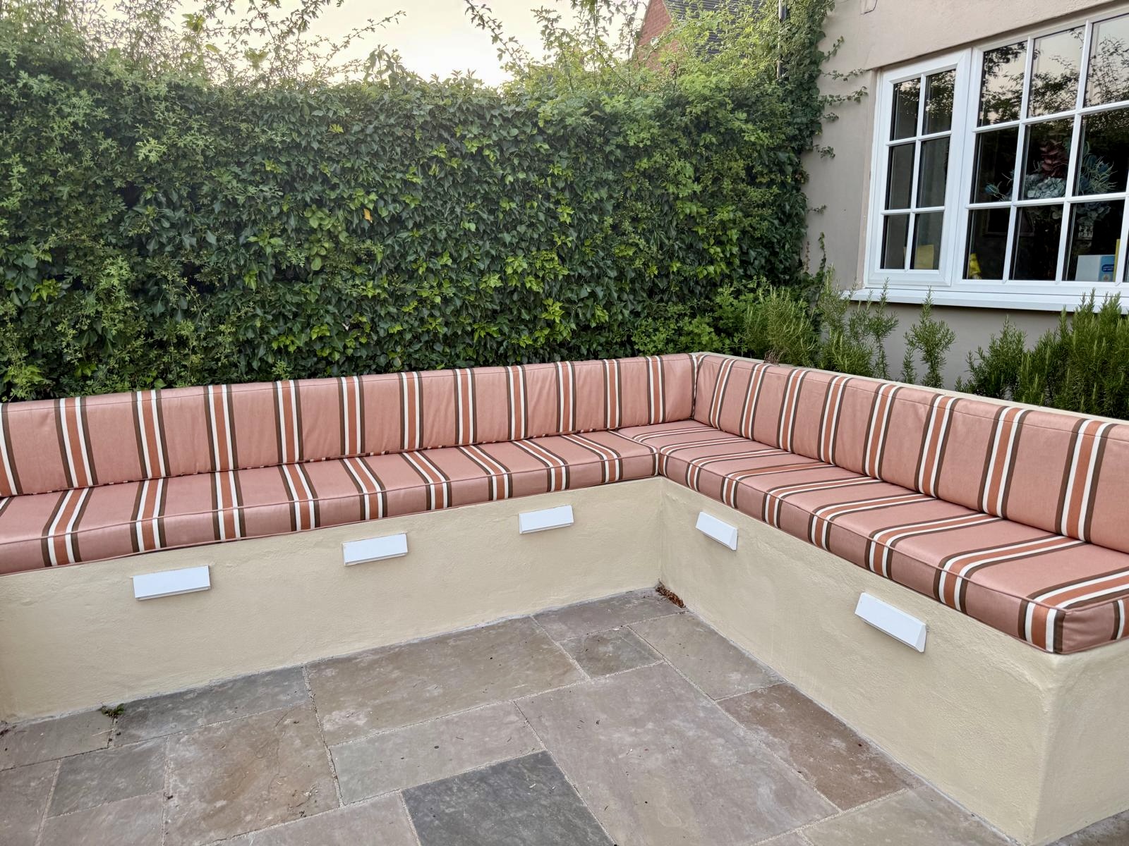 Bespoke outdoor bench seating cushions in striped fabric for an L-shaped built-in garden seating area.
